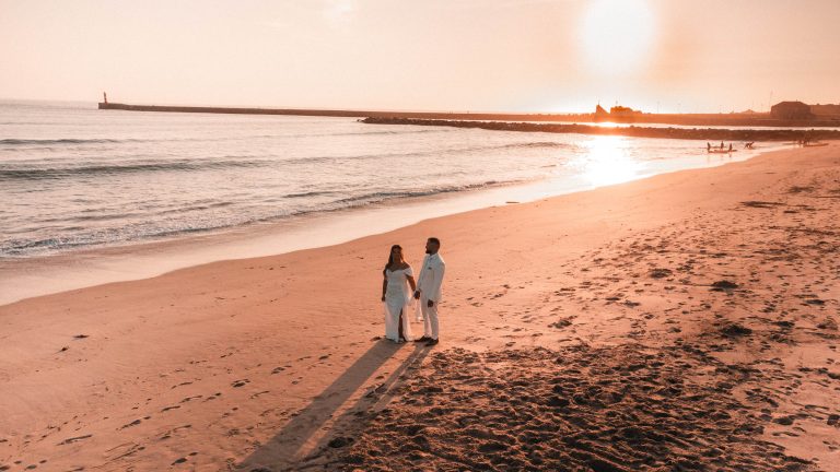 Noivos de mãos dadas na praia com o pôr-do-sol