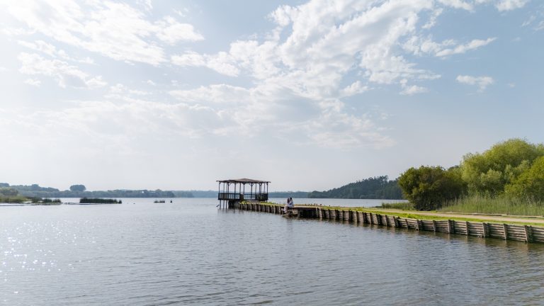 Casal sentado à beira rio com coreto de fundo