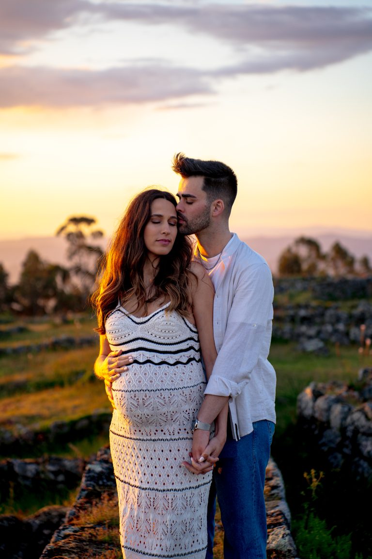 Casal abraçado com a mão na barriga de grávida e fundo de pôr-do-sol