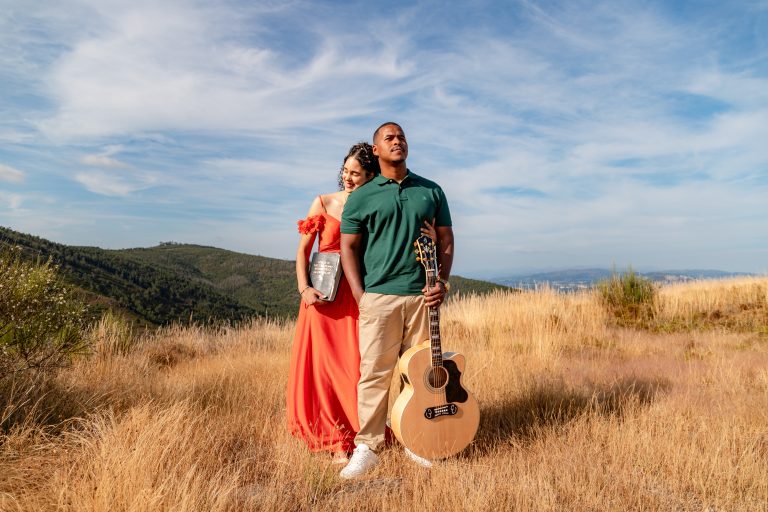 Casal abraçado com uma viola num campo